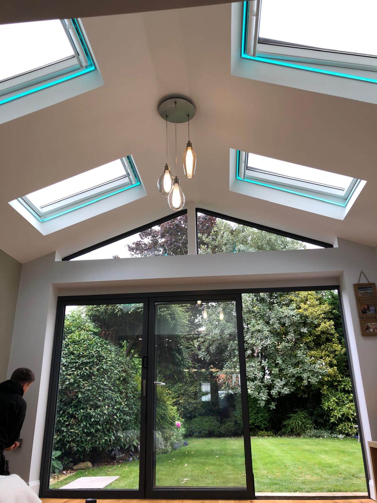 Modern sunroom extension with vaulted ceilings, skylights, and large bifold doors opening onto a lush green garden.